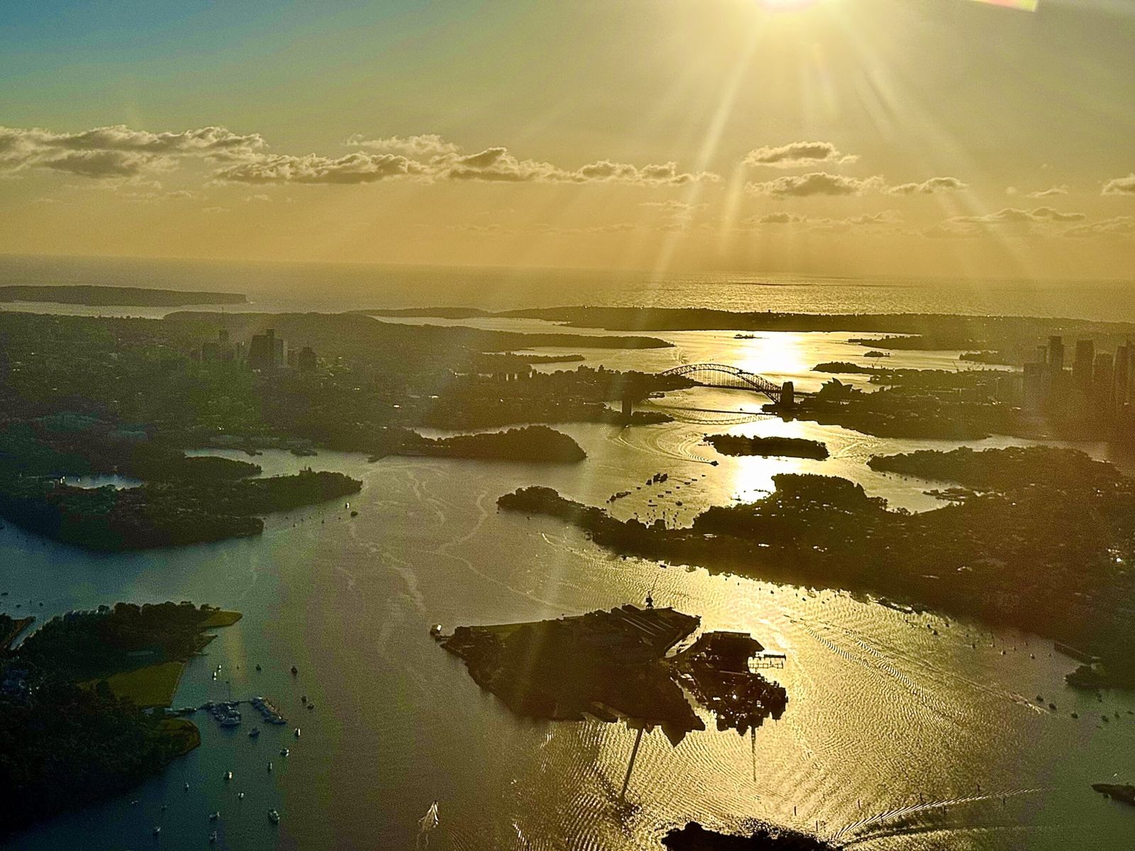 Early morning photo for the aircraft as we fly into Sydney the image shows the harbour and Harbour Bridge which is some glistening in Ray of the harbour. You can also see the city to the right and North Sydney to the left and the four shores of the suburbs surrounding the harbour. 