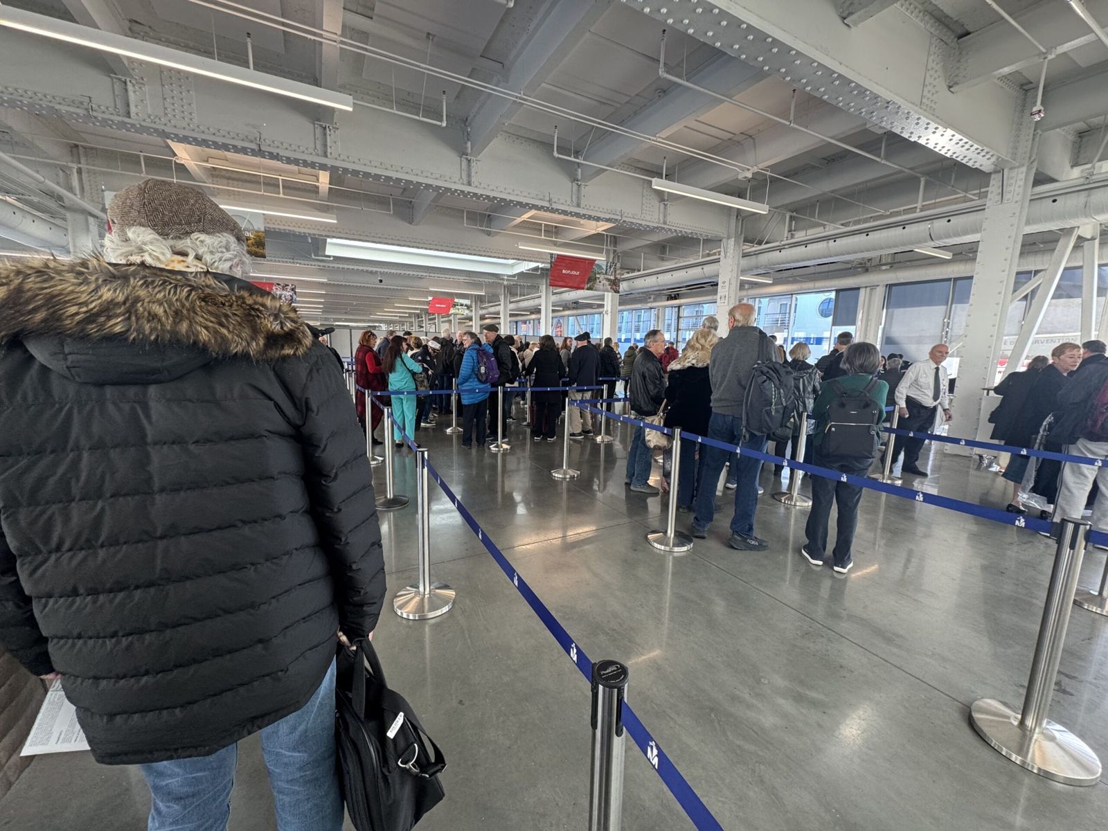 Our queue in the cruise terminal in Montreal. The room is large and people queue along rope lines. 