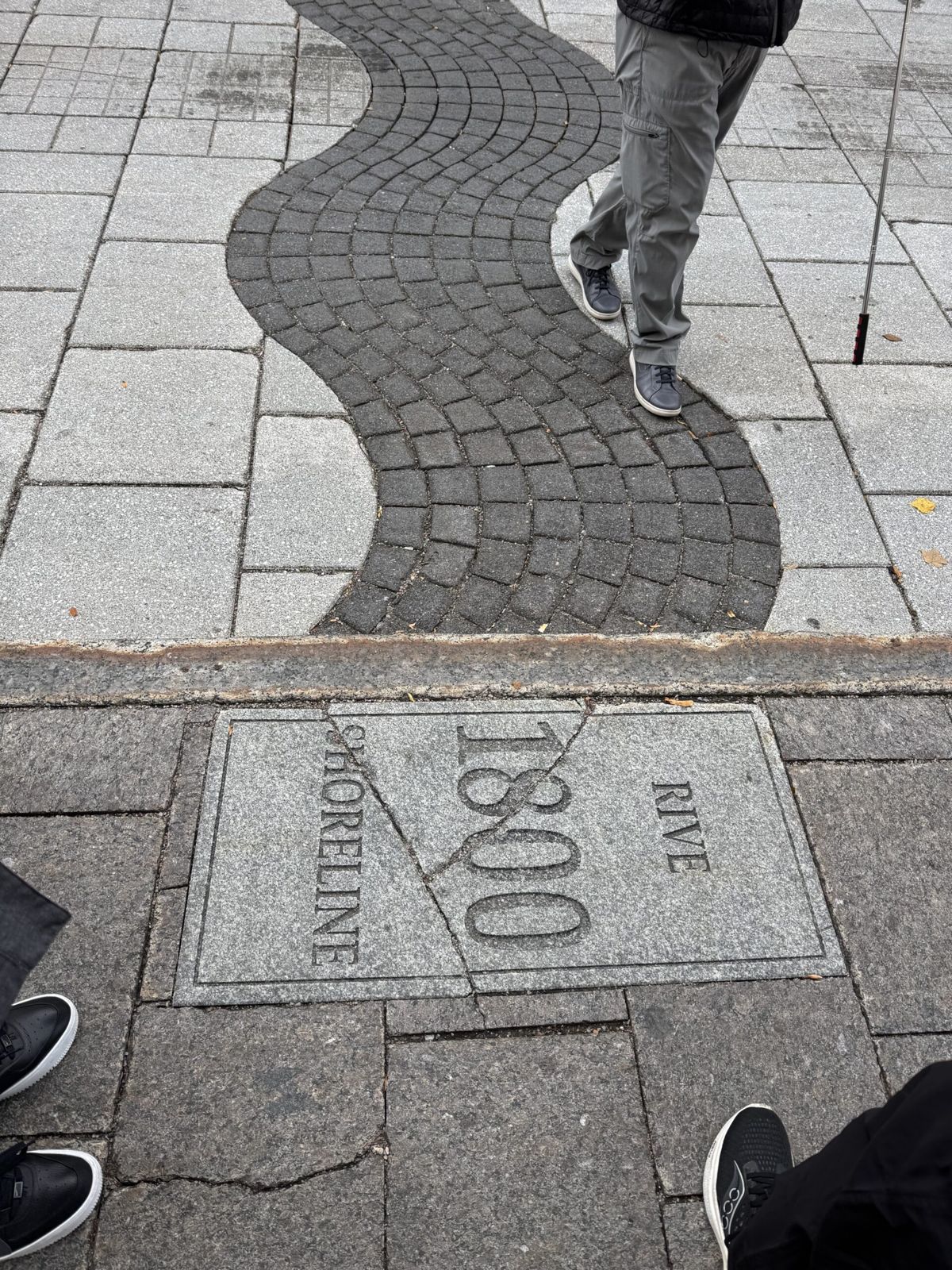A cobbled toad showing the numbers 1800.  The road has a wavy line of black stones surrounded by white. The wave represents the river bank in 1800. 