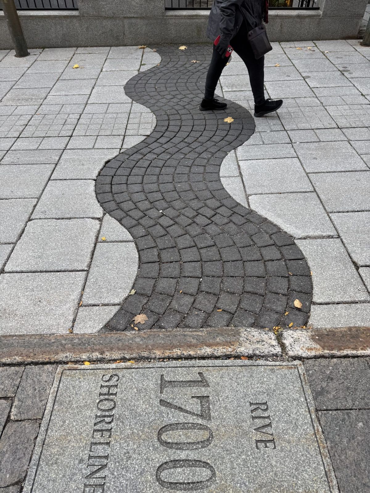 A cobbled toad showing the numbers 1700. The road has a wavy line of black stones surrounded by white. The wave represents the river bank in 1700.