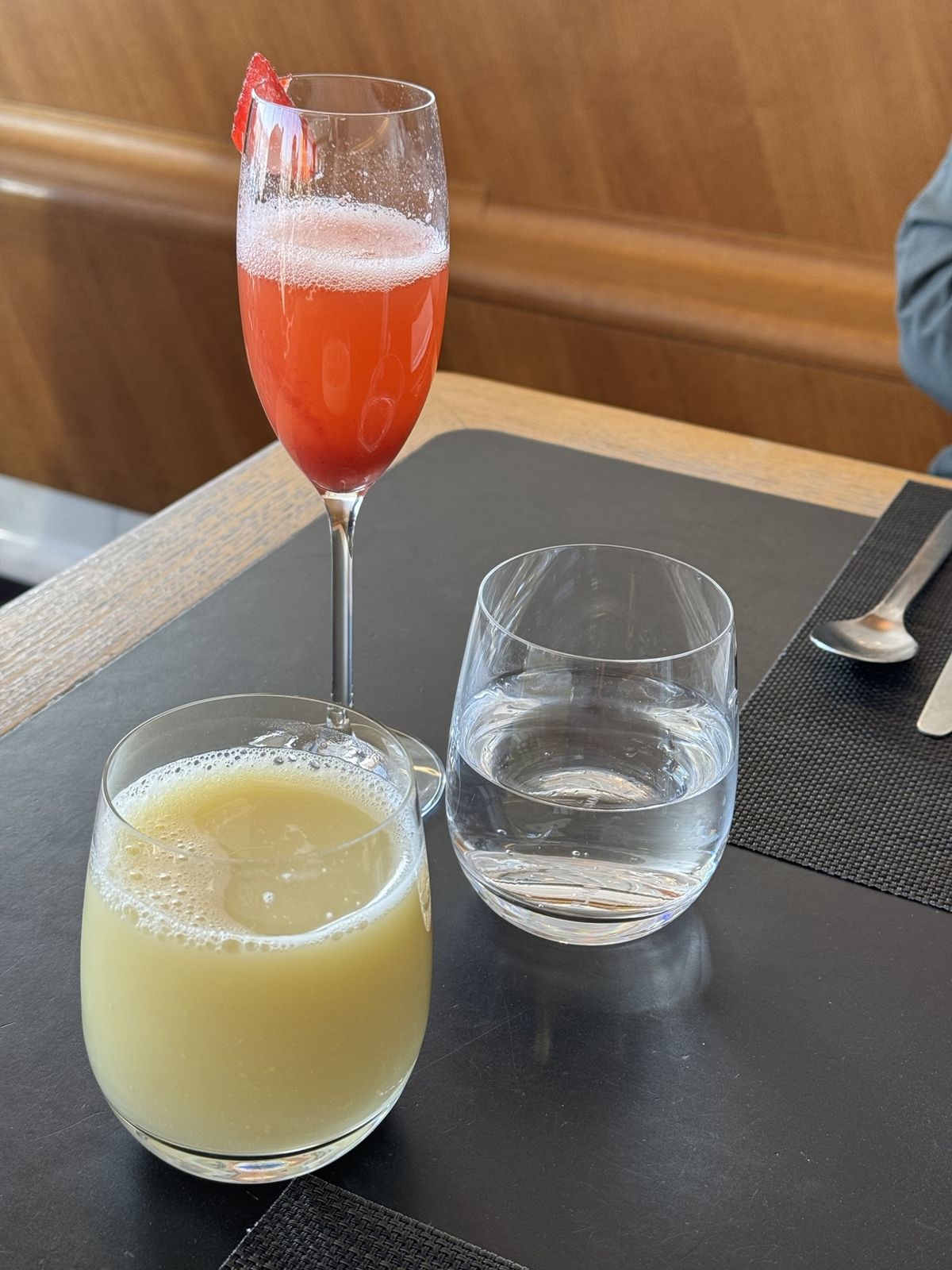 Three drinks sit on a table, a champagne cocktail with strawberry a glass of water and an apple and ginger juice