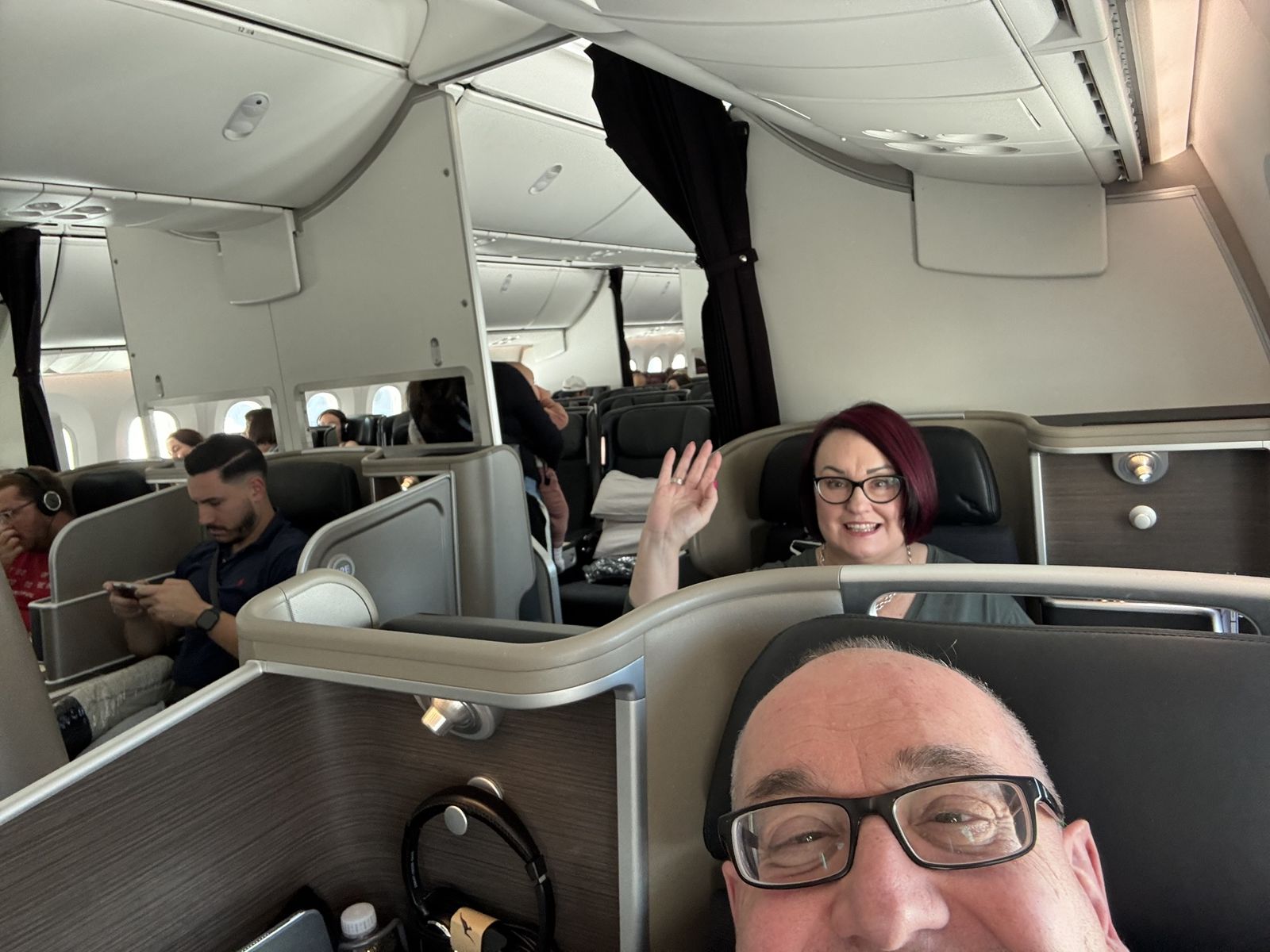 Michael is taking a selfie with himself and Mardi in the background in their seats on the 787 to New York