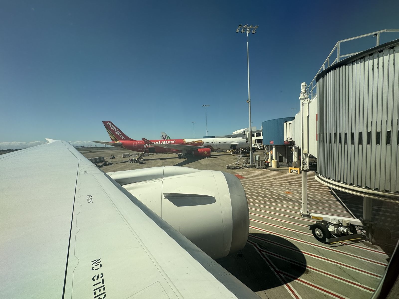 Wing and engine on the 787 as a taxi away from Sydney airport another aircraft is in thedistance. The sky is blue and it is a very sunny day