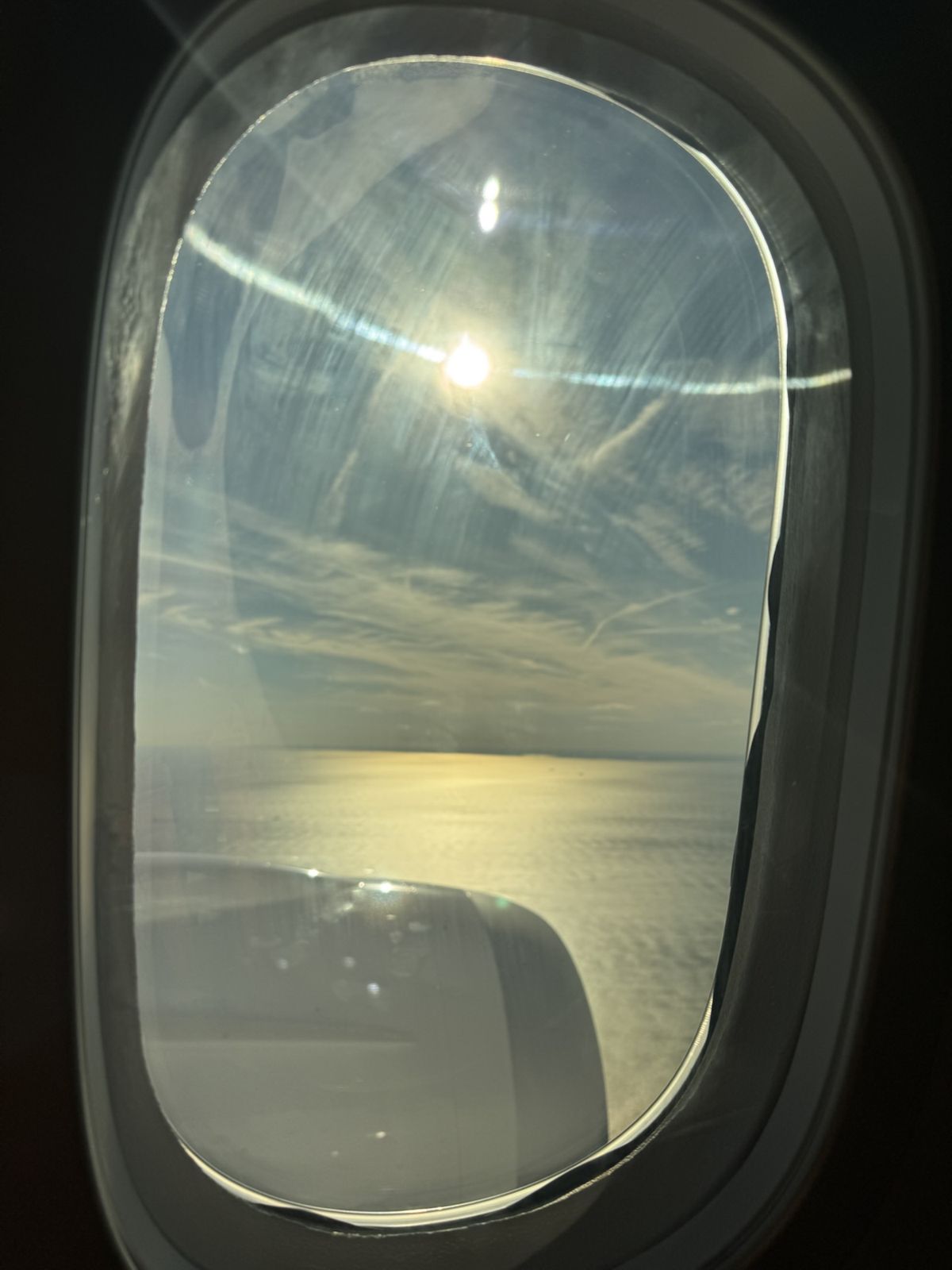 An image of the sun taken from inside the aircraft showing the wing and engine over the ocean