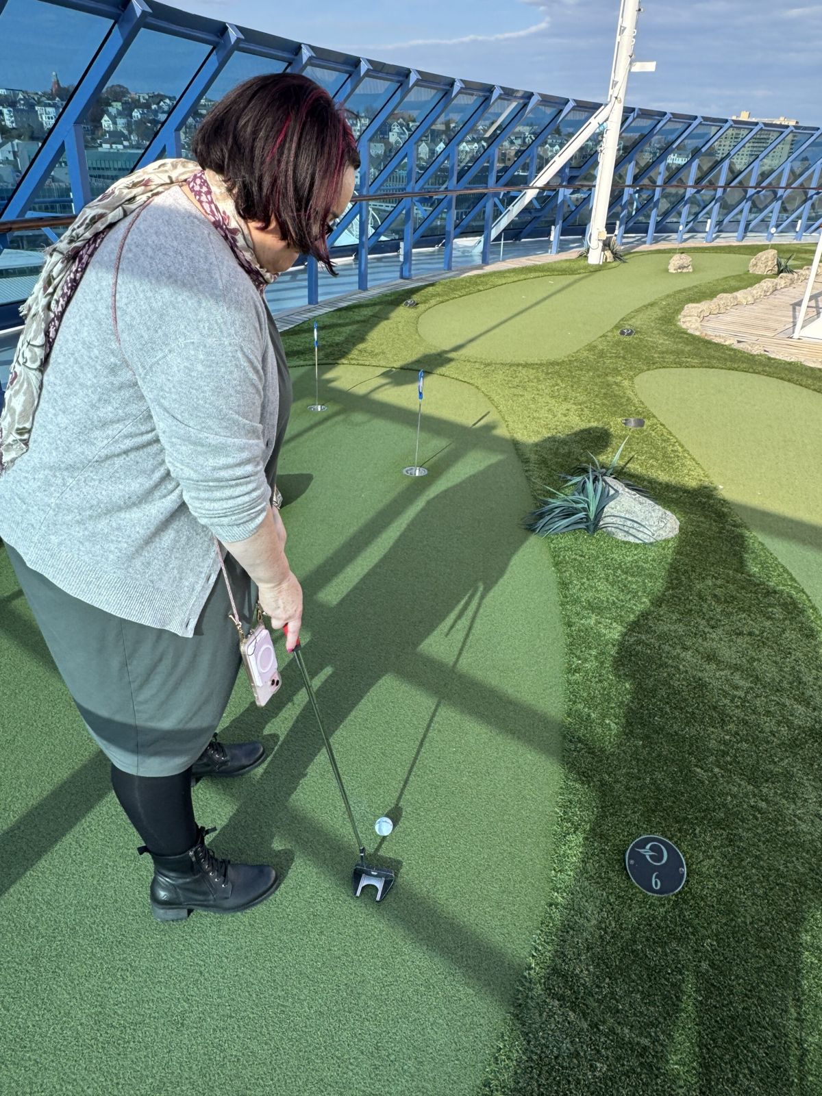 Mary putting on a green on the deck of insignia it’s bright and sunny. The hole is about 3 m from her. She’s about to take a stroke to the right as hazard.