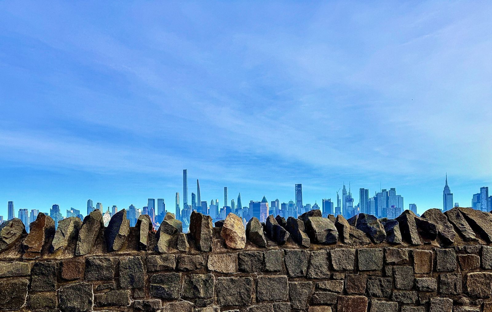 A view of manhattan, in the foreground a jagged rock fence frames the base of the image