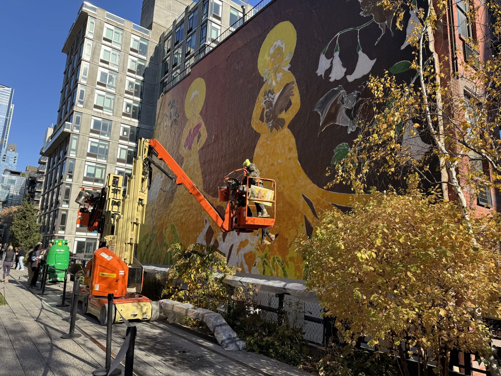 Artists painting a large mural on a wall. The mural appears to be of woman in period costume b